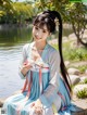 A woman in a blue and white dress sitting on a rock by the water.