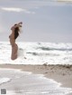 A woman in a bikini jumping in the air on a beach.