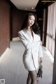 A woman in a white blazer and fishnet stockings posing for a picture.