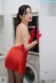 A woman in a red dress and red gloves standing in front of a washing machine.