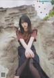 A woman sitting on top of a rock next to a rock wall.